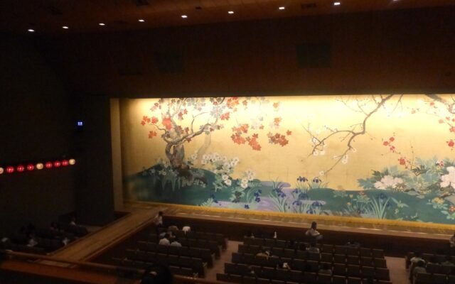 Plateia de teatro ocupada diante do pano de boca fechado, pintado com arvores e flores, antes do inicio do espetaculo.