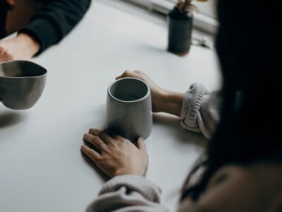 Duas pessoas sentadas à mesa segurando canecas, com os rostos fora do enquadramento