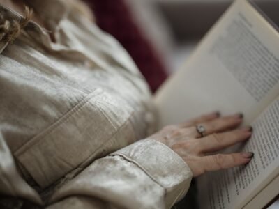Mão apoiada sobre a página aberta de um livro, em leitura tranquila dentro de casa
