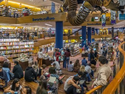 Interior de livraria com estantes altas cheias de livros e clientes circulando entre as prateleiras